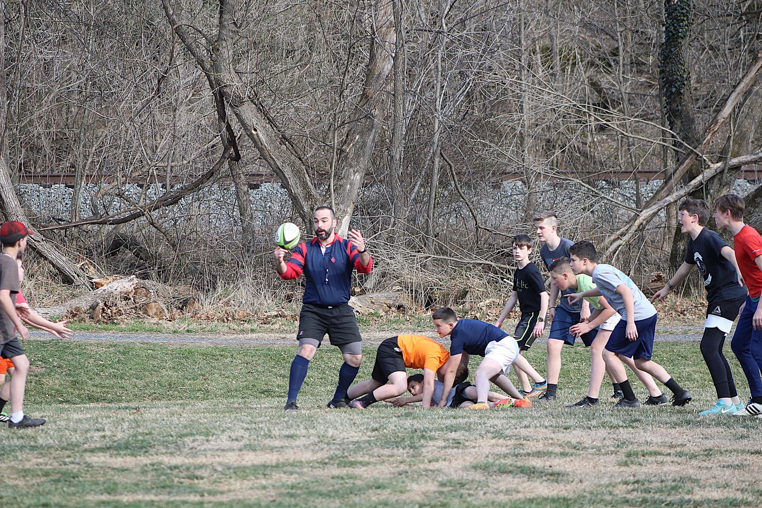 Sacred Heart Rugby players and a coach during a practice session on an open grass field.